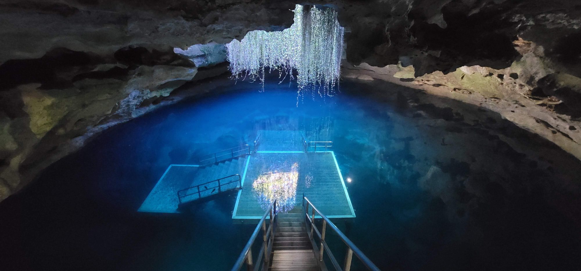 Devil's Den prehistoric spring near Williston, Florida — a shaft of daylight falls through the cavern roof onto the glowing blue water and submerged dive platform.