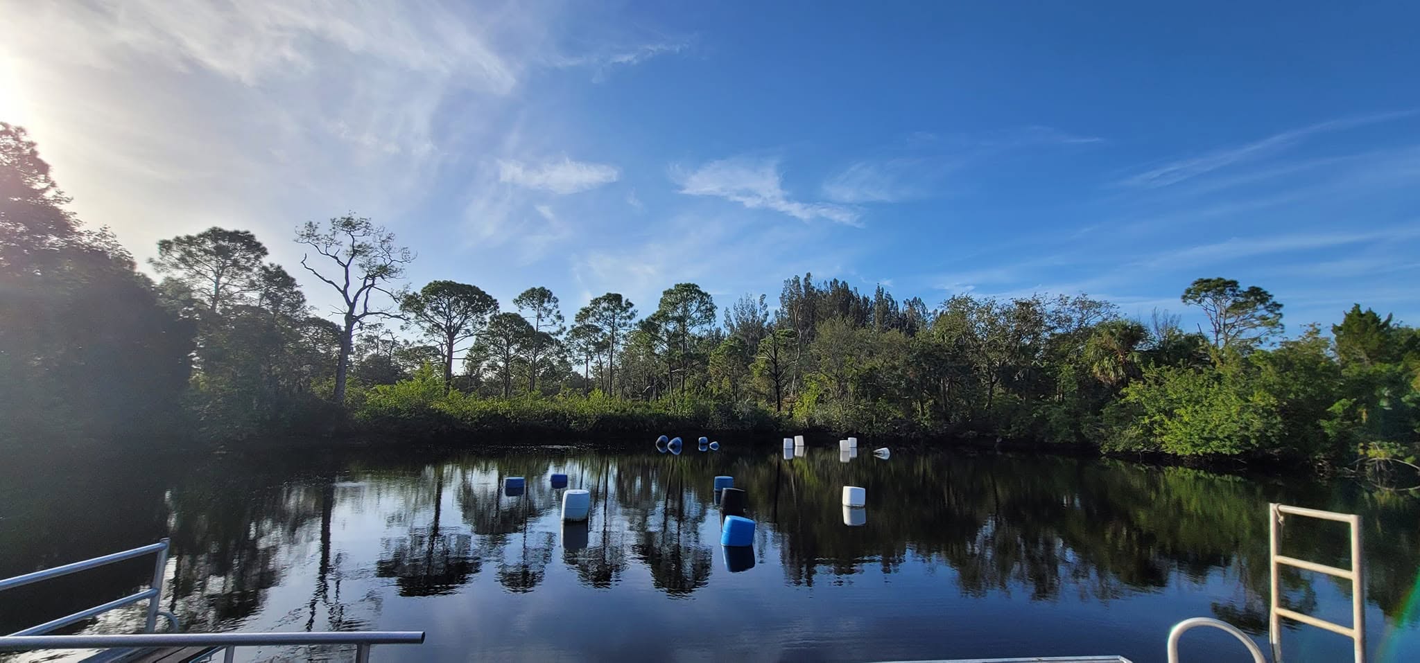 Hudson Grotto dive site in Hudson, Florida — calm, dark brackish water with surface floats marking submerged training platforms, ringed by trees at sunrise.
